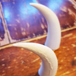 May include: Two white plastic horns, one lying down and one standing upright, on a wooden surface.