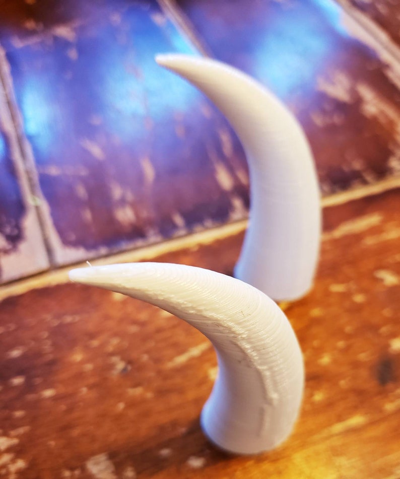 May include: Two white plastic horns, one lying down and one standing upright, on a wooden surface.