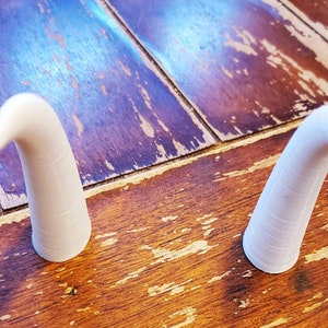 May include: Two white ceramic horns, each with a curved tip, are displayed on a wooden surface.