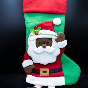 Könnte beinhalten: Ein grüner und roter Weihnachtssocken mit einer schwarzen Weihnachtsmannfigur. Die Weihnachtsmannfigur trägt einen roten Anzug mit weißem Bart und einer weißen Bommelmütze.