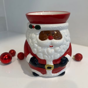 May include: A ceramic Santa Claus wax warmer with a red hat, white beard, and black face. The warmer has a red and black suit with a gold belt buckle.