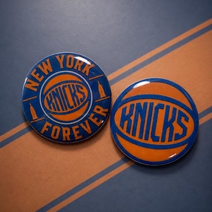 Può includere: Due spille circolari in smalto con il marchio della squadra di basket New York Knicks. Una spilla mostra il testo New York Forever con una grafica a forma di pallone, l'altra presenta la parola Knicks in lettere blu su un pallone arancione.