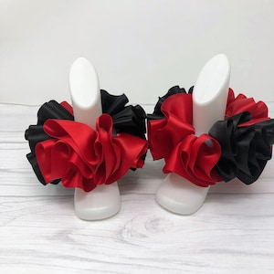 Könnte beinhalten: Ein Paar rote und schwarze, gekräuselte Stoff-Armbänder. Die Armbänder sind aus Satinband gefertigt und mit einer Schleife zusammengebunden.