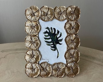 May include: A gold picture frame with a raised floral design surrounds a painting of a green leaf. The painting is signed "Aida Liver '90".