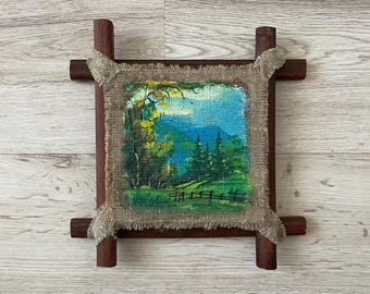 Könnte beinhalten: Ein gerahmtes Gemälde einer Landschaftsszene mit grünen Bäumen, blauem Himmel und einem Holzrahmen. Das Gemälde ist auf grobem Leinenstoff montiert.