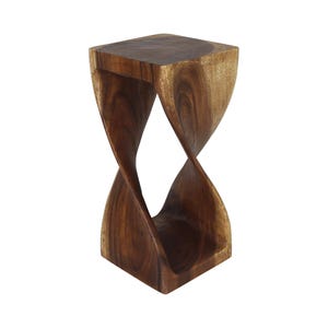 May include: A dark brown wooden stool featuring a square top and a square base connected by a central twisted, hourglass-shaped support structure. The wood grain is visible throughout the piece, showcasing natural patterns in the dark brown finish.