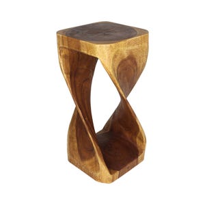 May include: A tall, hourglass-shaped wooden stool crafted from a single piece of natural wood. The stool features a smooth, flat square top and base connected by a central twisted, spiraling support structure with visible wood grain patterns.