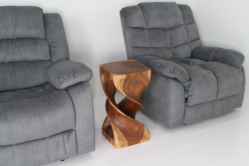 May include: A wooden end table with a unique twisted design. The table is made of dark brown wood and has a natural finish. It is sitting in front of two gray reclining chairs.