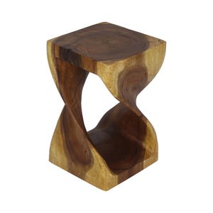 May include: A brown wooden stool featuring a square top and base connected by a central twisted, hourglass-shaped support. The natural wood grain displays varied light and dark brown tones throughout the entire structure of the piece.