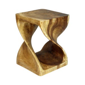 May include: A square-topped stool carved from a single piece of light and dark brown wood. The base and top are connected by a central twisted, hourglass-shaped support structure that features visible wood grain patterns throughout the surface.