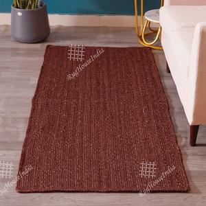 May include: A rectangular, dark brown woven area rug with a textured, braided surface. The rug features a consistent, deep earthy tone throughout its entire length and width, showcasing a dense, natural fiber construction with visible weave patterns.
