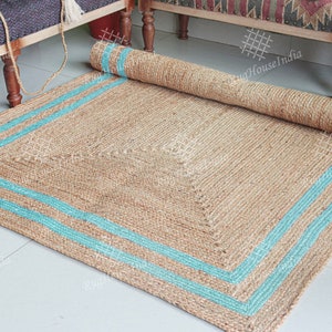 May include: A natural fiber rug with a square shape and a light brown color. The rug has a blue border with two stripes around the edges.