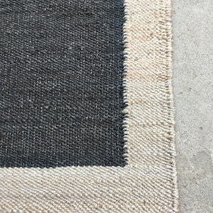 May include: A black and white rug with a woven texture. The rug has a black center and a white border.