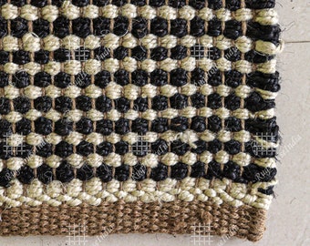 May include: Close-up of a black and beige woven rug with a brown border. The rug has a geometric pattern and is made of natural fibers.