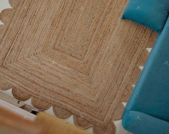 Könnte beinhalten: Ein natürlicher Jute-Teppich mit einem gewellten Rand und einem quadratischen Mitteldesign. Der Teppich hat eine hellbraune Farbe und befindet sich neben einem tealblauen Sofa und Kissen.