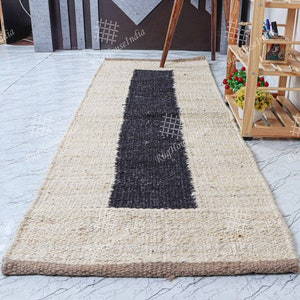 May include: A natural fiber rug with a black stripe down the center. The rug is made of jute and has a natural beige color. The rug is approximately 2.5 feet wide and 8 feet long.