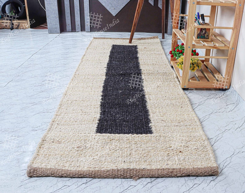 May include: A natural fiber rug with a black stripe down the center. The rug is made of jute and has a natural beige color. The rug is approximately 2.5 feet wide and 8 feet long.