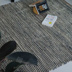 May include: A rectangular area rug featuring a woven texture with alternating thin stripes of black and off-white yarn. The rug is displayed with two books titled Think and Grow Rich and How to Win Friends and Influence People resting on its surface.
