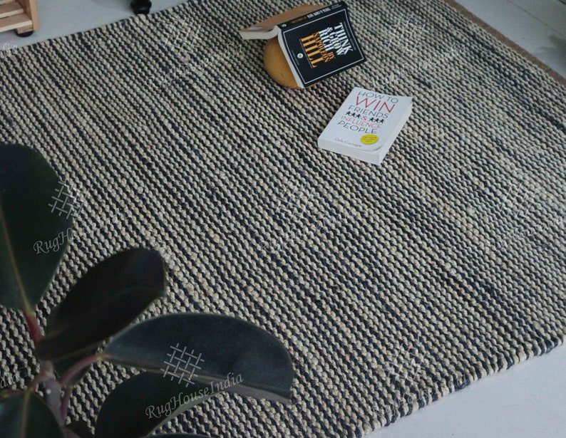 May include: A rectangular area rug featuring a woven texture with alternating thin stripes of black and off-white yarn. The rug is displayed with two books titled Think and Grow Rich and How to Win Friends and Influence People resting on its surface.