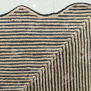 May include: A black and natural jute rug with a wavy edge and a striped pattern. The rug is made of natural fibers and has a rustic look.