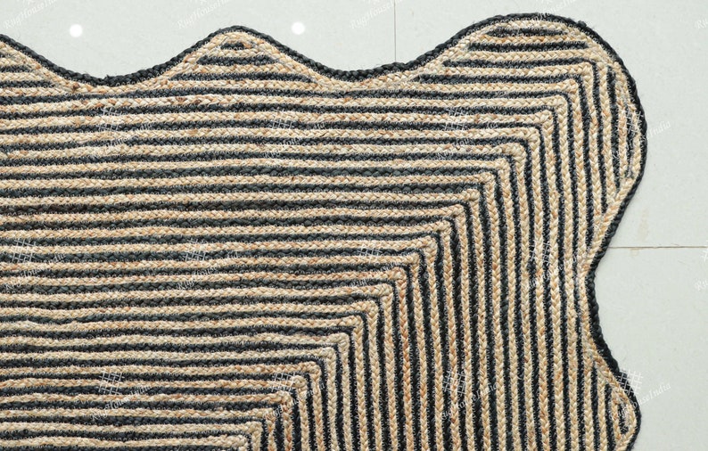 May include: A black and natural jute rug with a wavy edge and a striped pattern. The rug is made of natural fibers and has a rustic look.