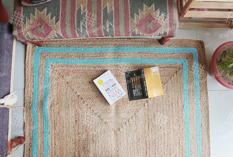 May include: A light blue and brown jute rug with a light blue border. Two books are on the rug, one is yellow and the other is black. The yellow book has the text 'HOW TO WIN FRIENDS & INFLUENCE PEOPLE' and the black book has the text 'THINK SLOW, ACT FAST.'