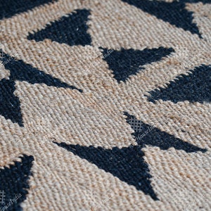 Puede incluir: Primer plano de una alfombra de fibra natural con un patr&oacute;n geom&eacute;trico de tri&aacute;ngulos negros sobre un fondo beige. La alfombra est&aacute; tejida con una superficie texturizada, ligeramente rugosa.