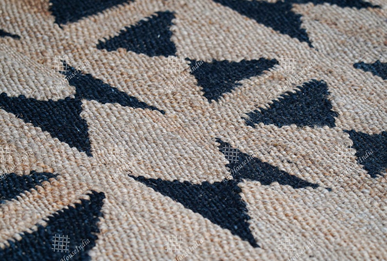 Puede incluir: Primer plano de una alfombra de fibra natural con un patr&oacute;n geom&eacute;trico de tri&aacute;ngulos negros sobre un fondo beige. La alfombra est&aacute; tejida con una superficie texturizada, ligeramente rugosa.
