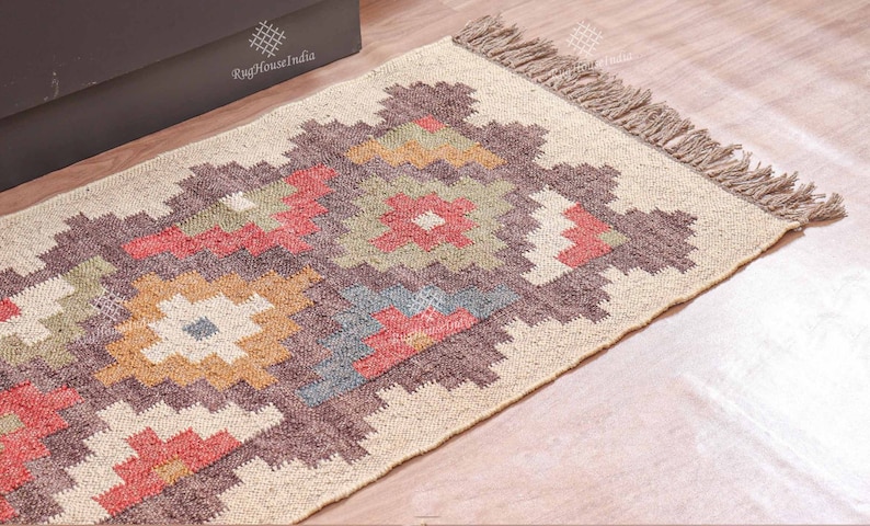 May include: A beige and brown geometric patterned rug with a fringe border. The rug has a cream background with brown, red, and green geometric shapes.