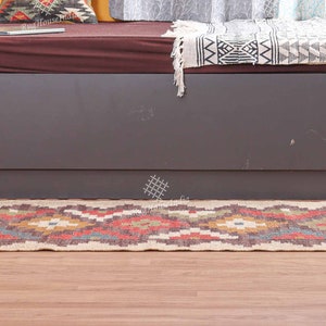 May include: A brown and beige patterned jute rug with fringe on the ends. The rug is laid out on a wooden floor in front of a gray couch and a teal stool.
