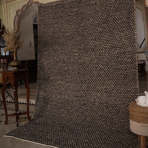 May include: A large, rectangular area rug with a textured, woven design in shades of brown and beige. The rug is displayed indoors, with a white border and a neutral background. The rug's pattern is consistent across its surface.