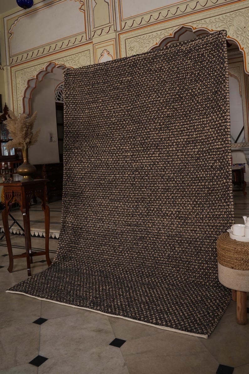 May include: A large, rectangular area rug with a textured, woven design in shades of brown and beige. The rug is displayed indoors, with a white border and a neutral background. The rug's pattern is consistent across its surface.