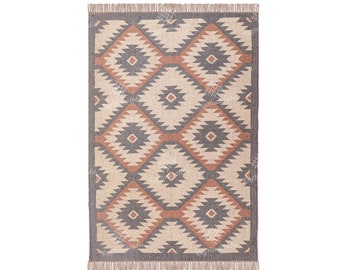 Puede incluir: Una alfombra rectangular con un patrón geométrico en tonos marrones, beige y grises. La alfombra tiene un borde de flecos.