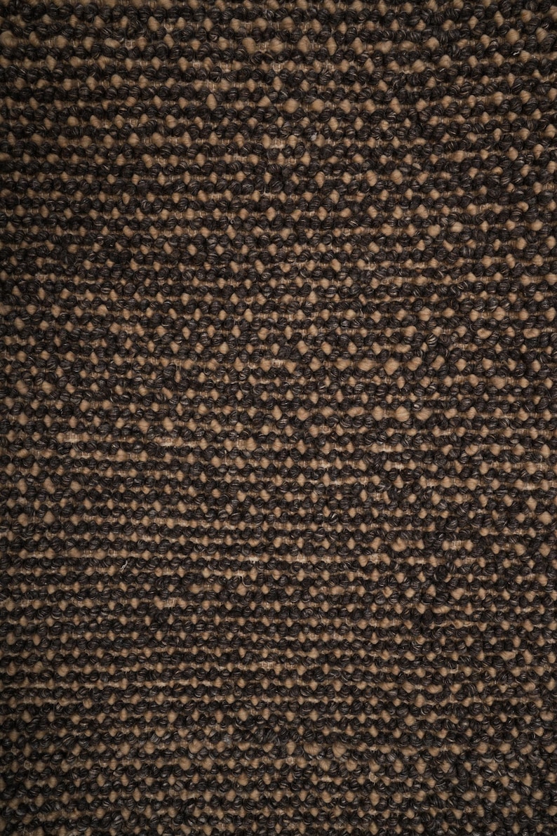 May include: Close-up of a textured, woven fabric with a speckled pattern. The fabric features a dark brown color with lighter tan-colored flecks throughout, creating a contrasting visual effect. The weave appears tight and durable.