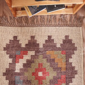 May include: A brown and beige rug with a geometric pattern in shades of red, orange, green, and blue. The rug has a fringe border.
