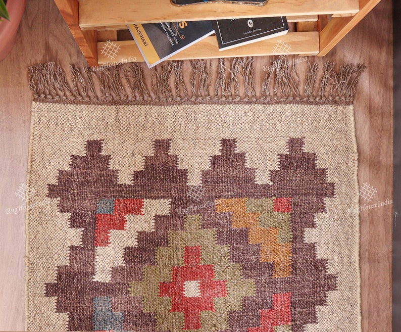 May include: A brown and beige rug with a geometric pattern in shades of red, orange, green, and blue. The rug has a fringe border.