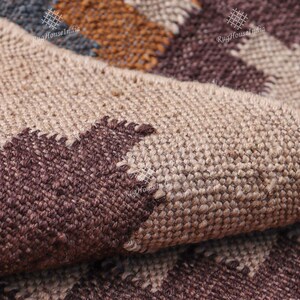 May include: Close-up of a woven rug with a geometric pattern in shades of brown, beige, and blue. The rug is made of natural fibers and has a textured surface.