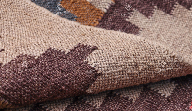 May include: Close-up of a woven rug with a geometric pattern in shades of brown, beige, and blue. The rug is made of natural fibers and has a textured surface.