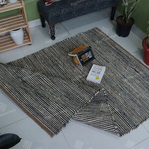 May include: A rectangular area rug featuring a woven pattern of alternating dark navy blue and off-white stripes. The rug has a thick, textured appearance with a brown fabric border along the edges. Two books are placed on the surface of the rug.
