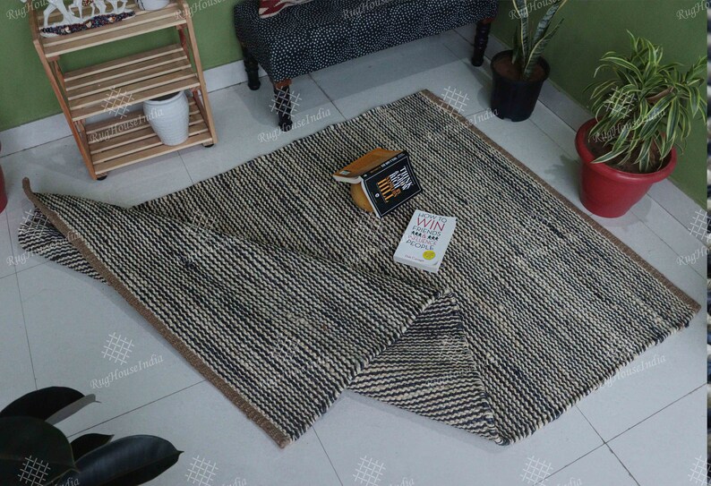 May include: A rectangular area rug featuring a woven pattern of alternating dark navy blue and off-white stripes. The rug has a thick, textured appearance with a brown fabric border along the edges. Two books are placed on the surface of the rug.