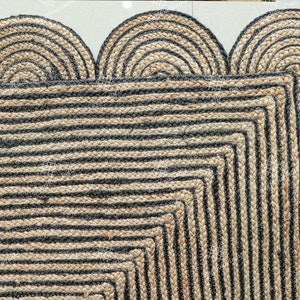 May include: A black and natural jute rug with a geometric pattern and a scalloped edge. The rug is made of natural fibers and has a rustic look.