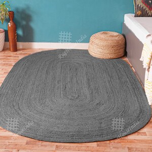 May include: An oval-shaped area rug in a solid dark gray color, featuring a braided texture constructed from concentric loops. The rug is positioned flat on a wooden floor, showcasing a consistent woven pattern throughout its entire surface area.