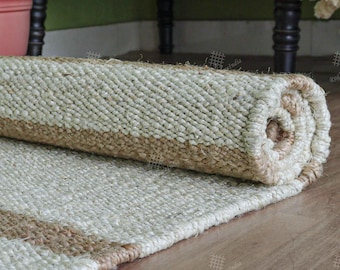 May include: A close-up of a rolled-up natural fiber rug with a light beige and brown striped pattern. The rug is made of jute and is perfect for adding a touch of natural texture to any room.