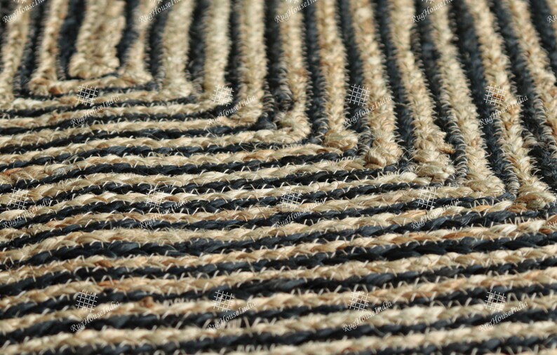 May include: Close-up of a black and natural jute rug with a geometric pattern. The rug is made of woven strands of jute and black yarn.