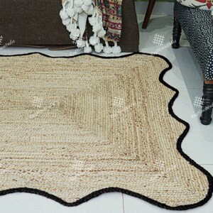 May include: A natural fiber rug with a wavy, black border. The rug is made of woven jute and has a light brown color.