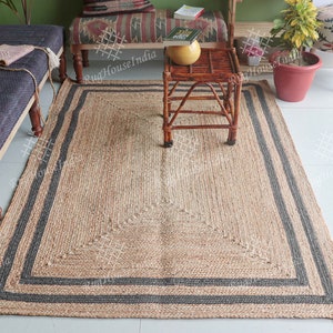 May include: A natural fibre rug with a black border. The rug is made of jute and has a woven texture. The rug is rectangular and has a fringed edge.
