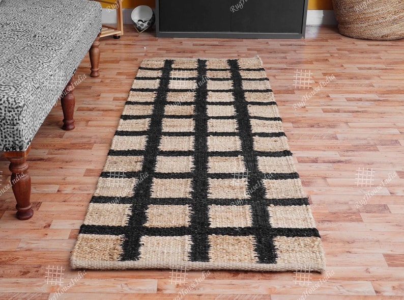 Puede incluir: Una alfombra de fibra natural con un patr&oacute;n de cuadros negros y beige. La alfombra est&aacute; hecha de yute y es perfecta para agregar un toque de textura natural a cualquier habitaci&oacute;n.