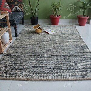May include: A rectangular area rug featuring a textured, hand-woven design with alternating horizontal stripes of dark navy blue and natural off-white fibers. The rug has a thick, braided construction with a visible jute-like border edge.