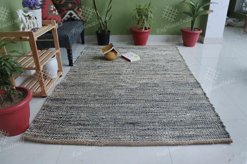 May include: A rectangular area rug featuring a textured, hand-woven design with alternating horizontal stripes of dark navy blue and natural off-white fibers. The rug has a thick, braided construction with a visible jute-like border edge.