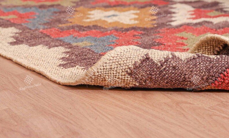 May include: Close-up of a brown, beige, and red patterned rug with a woven texture. The rug is rolled up and the edge is visible. The rug is on a wooden floor.